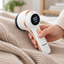 Elektrisk fnugfjerner i brug p� en beige striktr�je, hvor den fjerner fnuller og stofnupper.