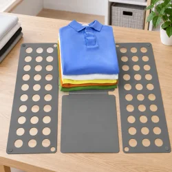 T�jfolder p� et bord med en stak foldede T-shirts placeret p� foldebr�ttet.